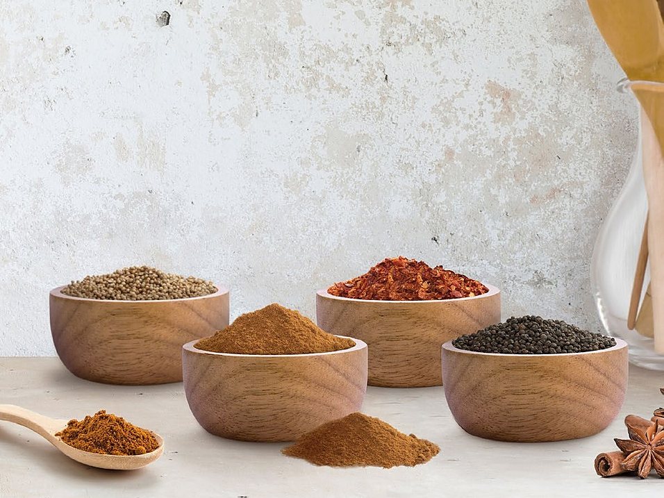 Wooden bowls of coriander seed, chilli flakes, black pepper and ground spices on a table